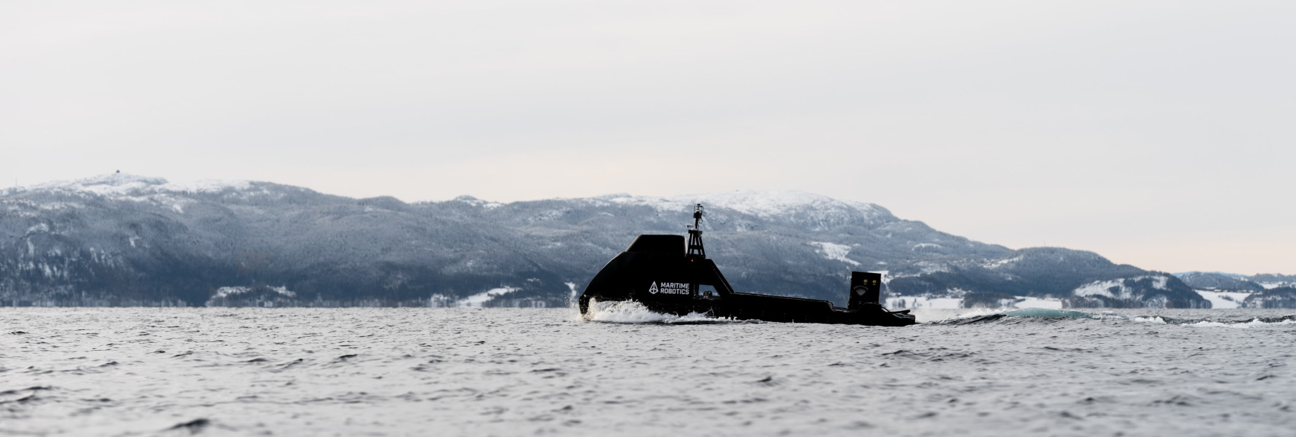 Side view of the Mariner X autonomous vessel navigating Norwegian waters with mountains in the background.