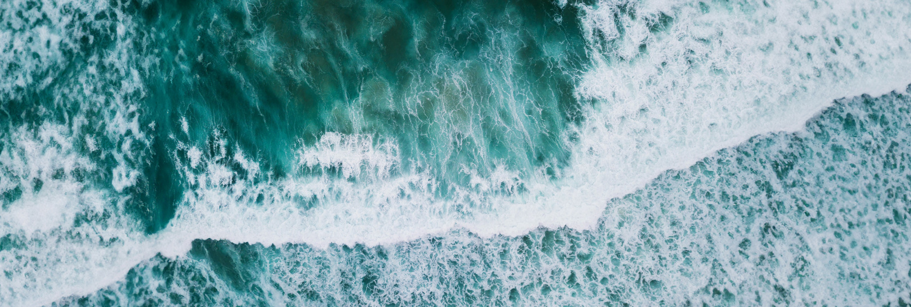 Aerial view capturing the hues of a blue-green ocean with rolling waves.