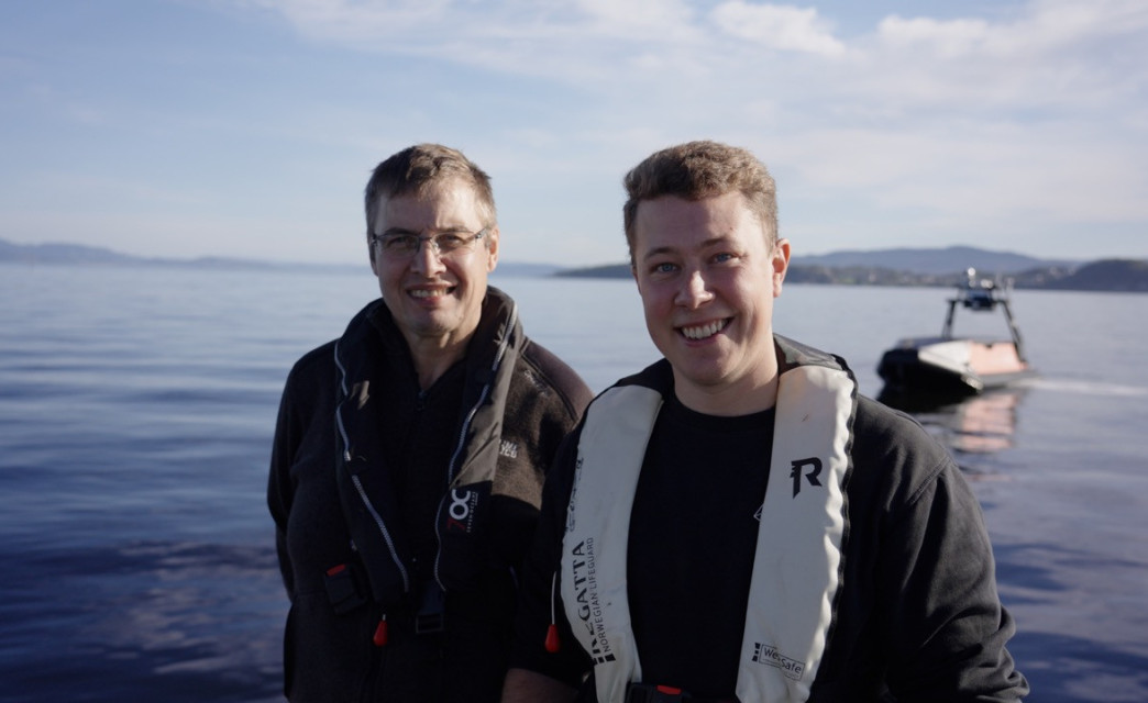 Two Maritime Robotics employees smiling with a Mariner USV in the background.